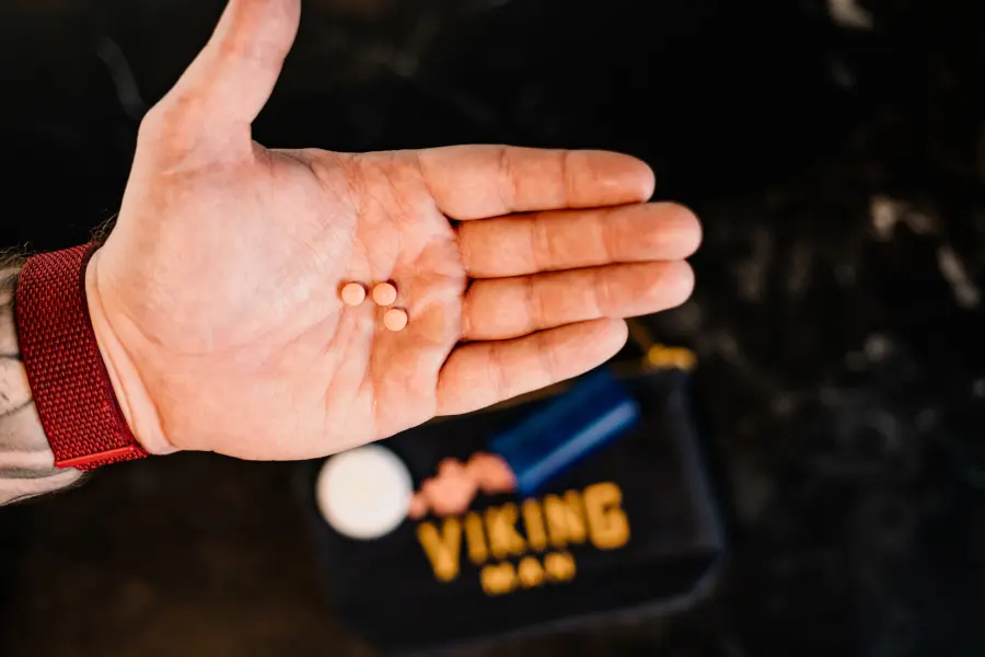 Man with open palm holding three pills. Viking Man packaging seen in the background.